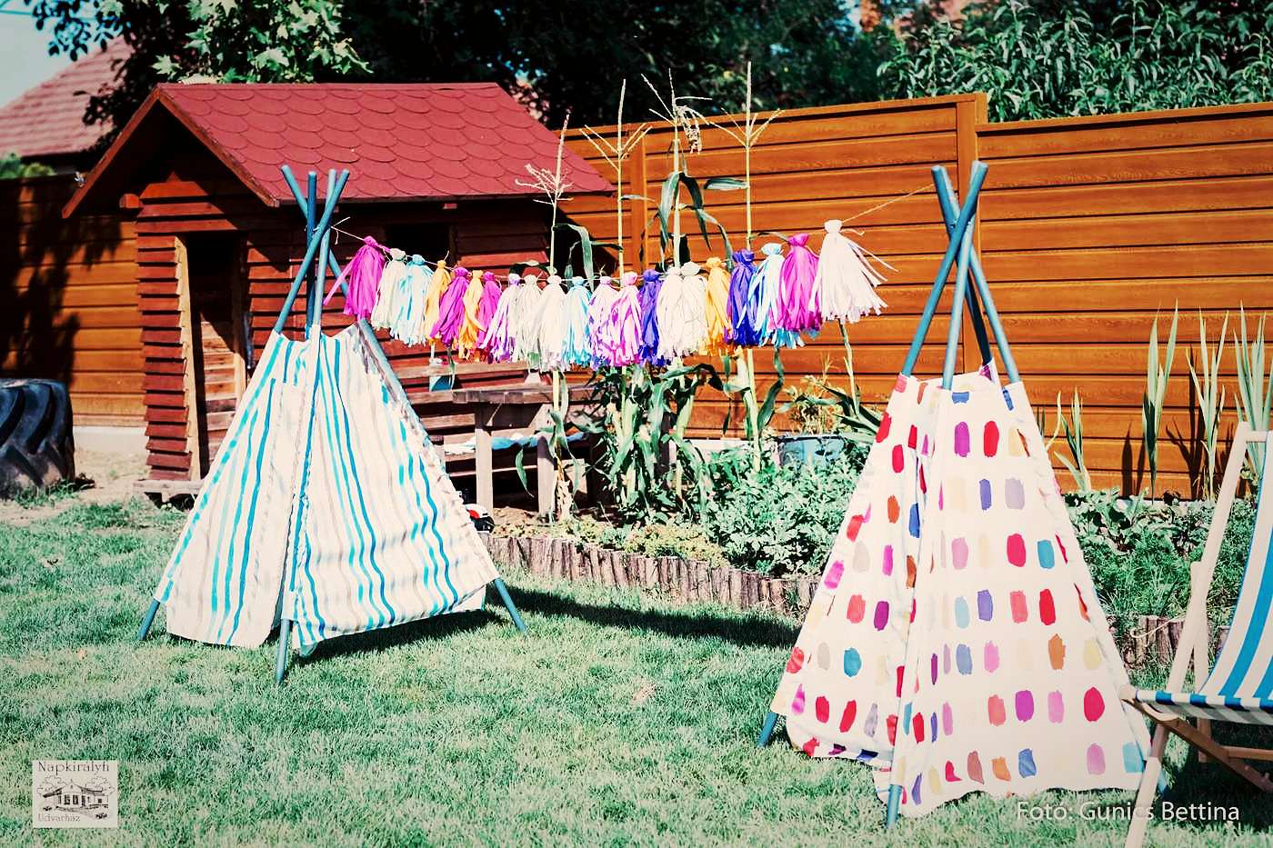 Színes tipi-sátrak és zászlófüzér a fűben, az udvarházi kertben